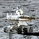A six-wheeled rover (Yutu-2) sits centrally on the grey background of the lunar surface.